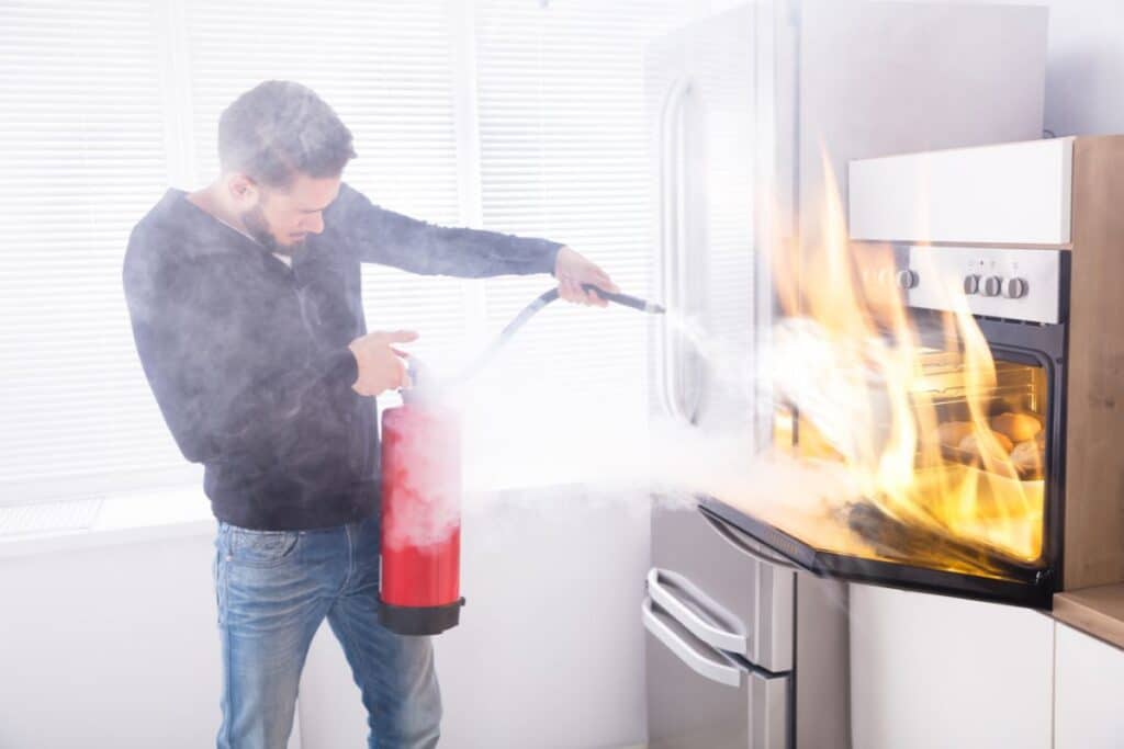man using a fire extinguisher to put out an oven fire.