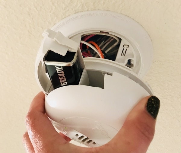 A hand opening a smoke alarm.