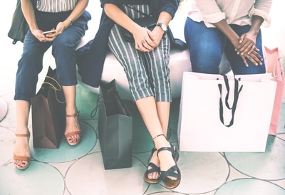 3 ladies sitting on a bench with shopping bags and purses.