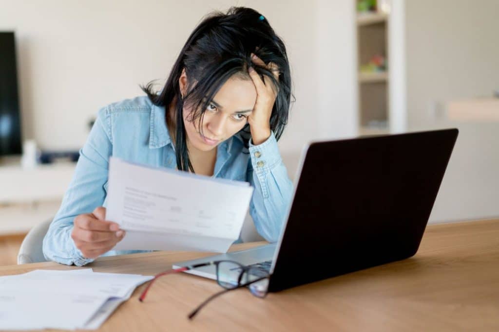 woman frustrated looking at paperwork and laptop