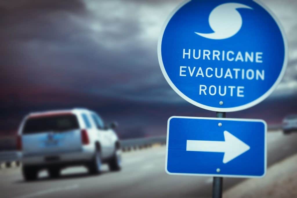 car driving under dark clouds past hurricane evacuation route sign