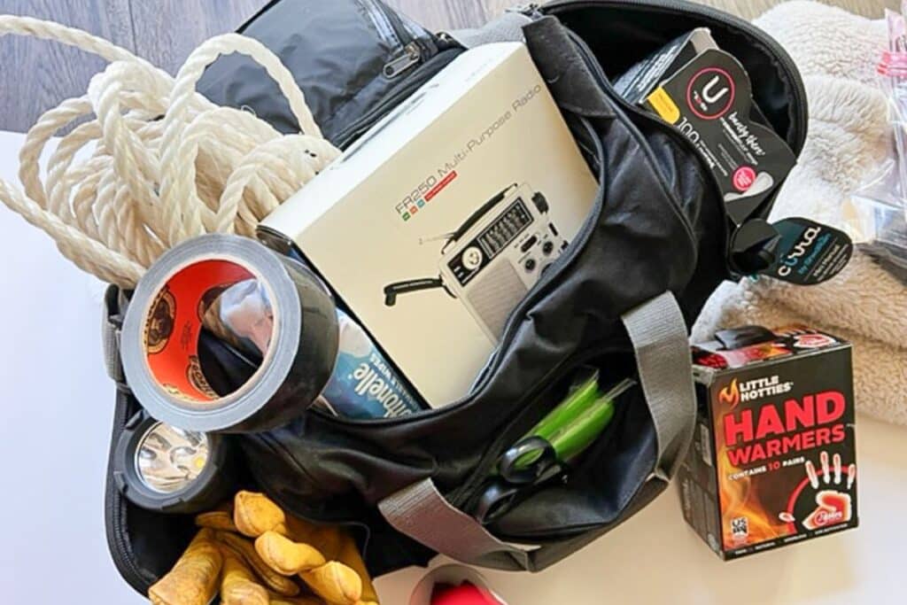 black duffel bag full of emergency car kit essentials like work gloves handwarmers and duct tape.