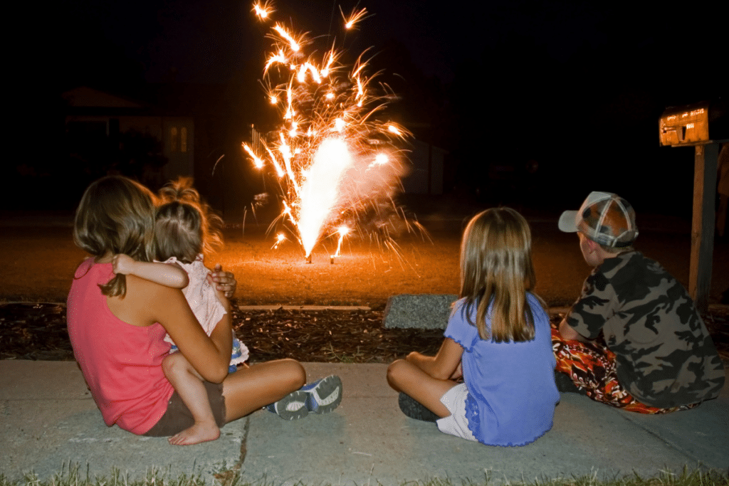 group of kids watching fireworks from a sidewalk.
